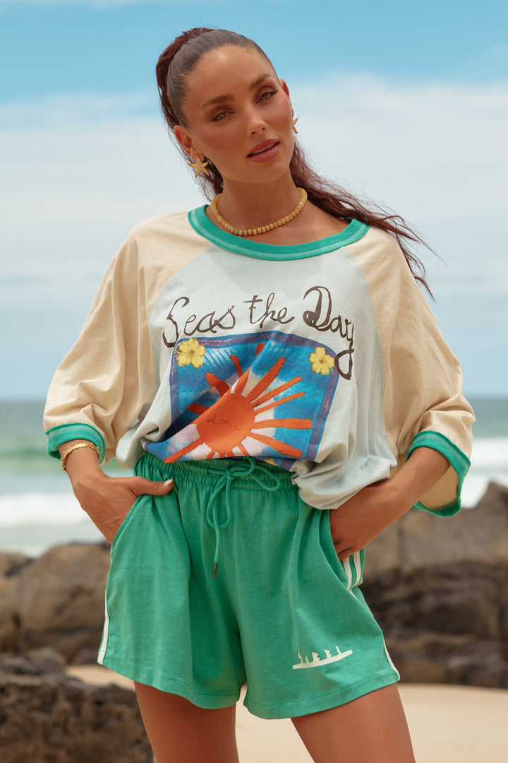 Woman wearing a colorful shirt and green shorts with a beach background