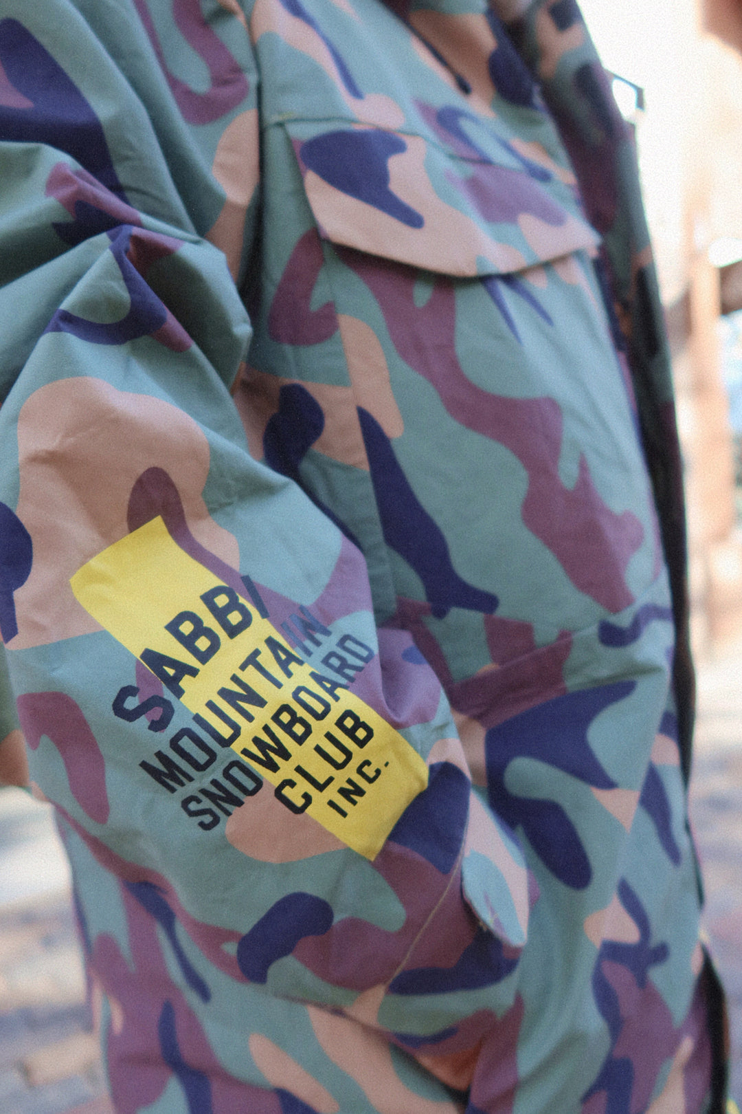 Camouflage jacket with a yellow label reading 'SABB Mountain Snowboard Club, Inc.'