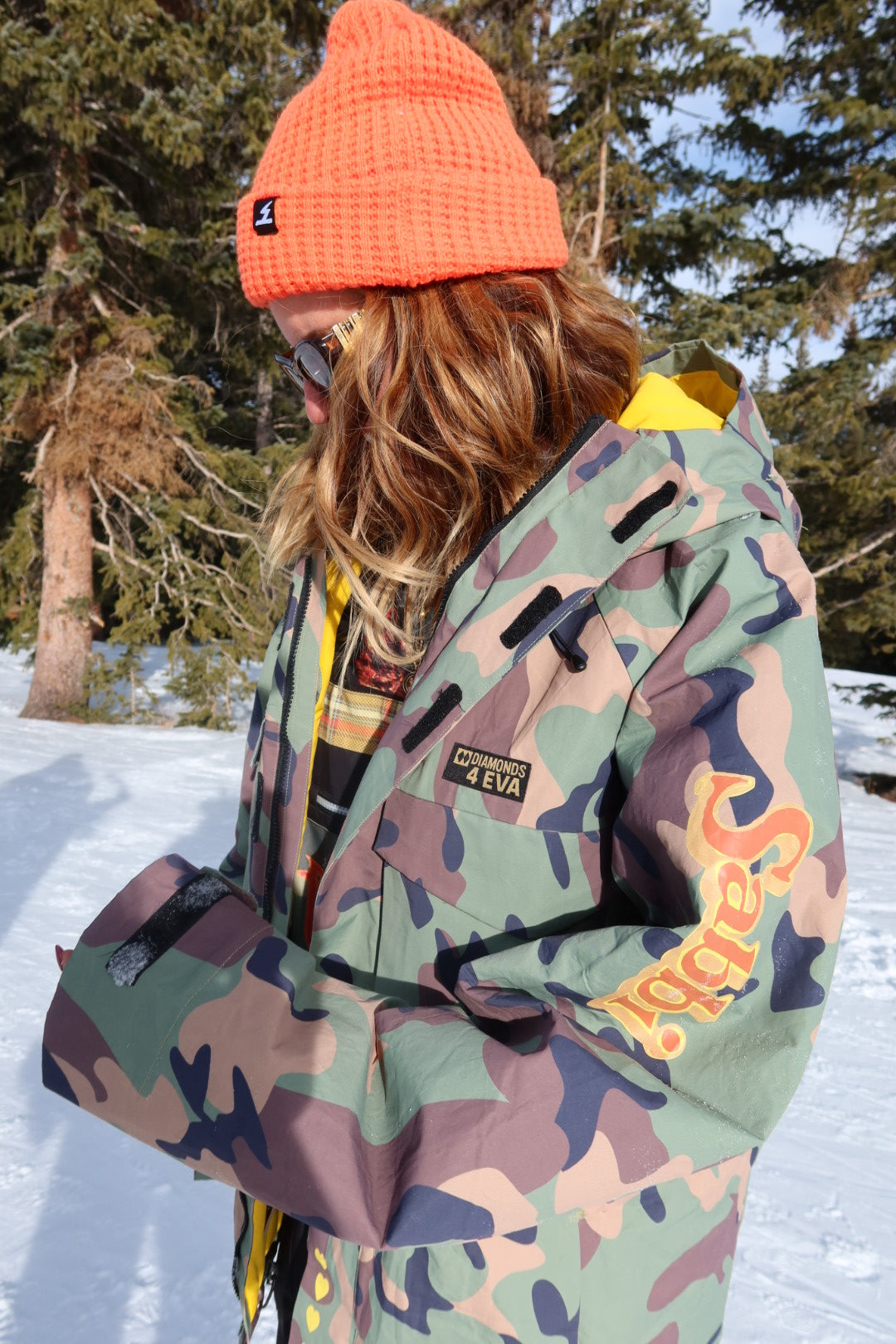 Person wearing a camouflage jacket with 'Sabbi' branding in a snowy outdoor setting