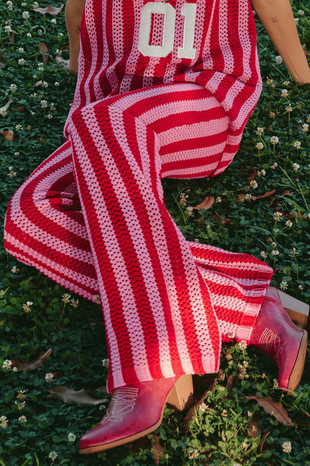 Person sitting on grass wearing red and pink Striped Knit Pants.